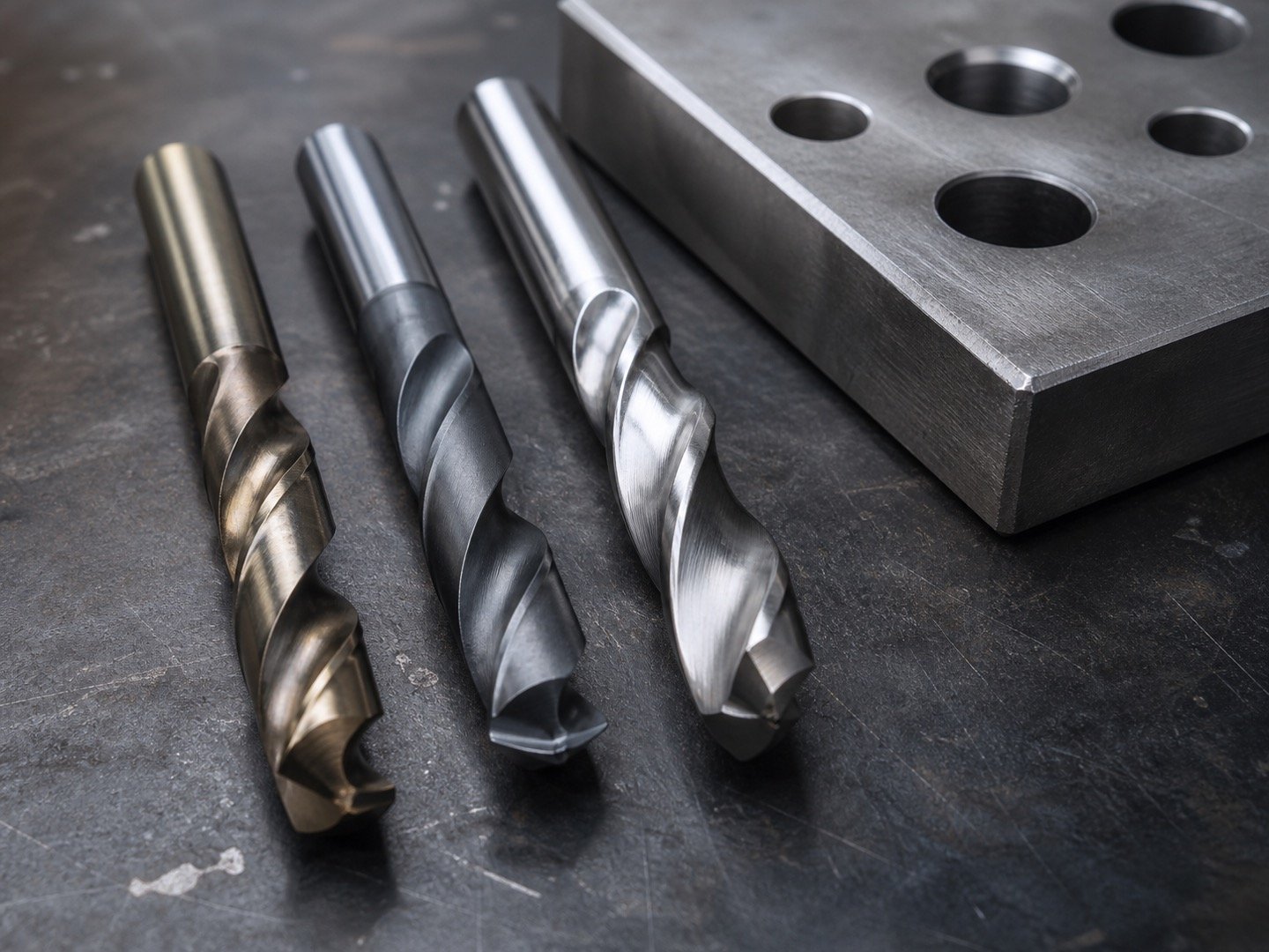 Cobalt and carbide twist drill bits beside a hardened steel plate with drilled holes